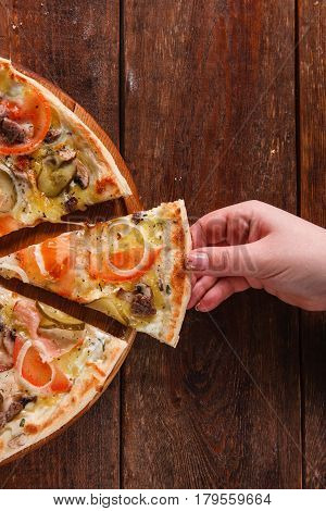 Italian fast food. Hand taking slice of fresh appetizing yummy pizza served on dark wooden table with free space for text.