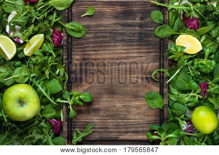 Green food background. Salad ingredients on table with copy space and cutting board for your text. Healthy food and diet concept.