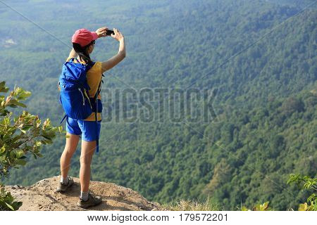 successful woman hiker taking photo with cellphone hiking on mountain peak