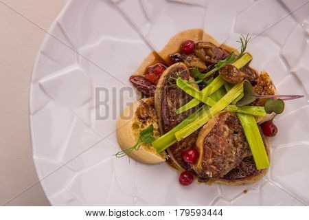 The fried goose liver with onions cake on a round white plate which costs on a table with a cloth