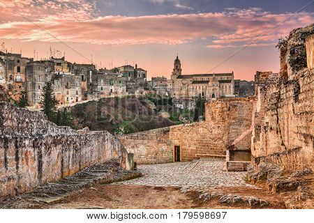 Gravina in Puglia, Bari, Italy: landscape at sunrise of the old town with the cathedral seen from the pathway with the source at the entrance of the ancient aqueduct bridge over the ravine
