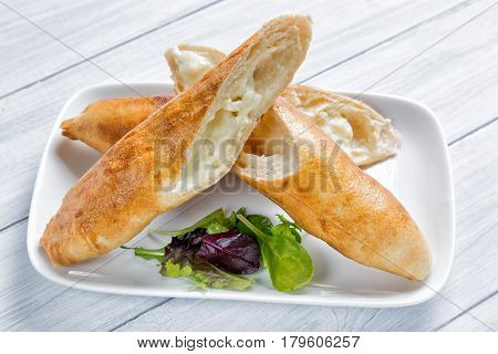 Abkhazian or Georgian national dish Khachapuri bread with cheese and salad on a plate and white wooden table.