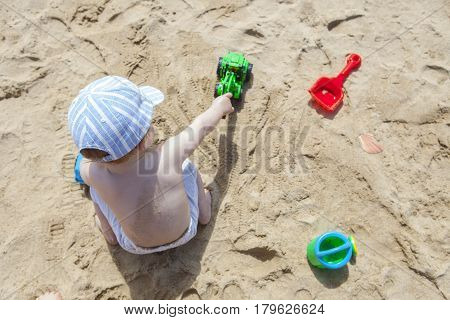 Baby boy playing on sand at the beach with toy backhoe watering can shovel and truck. El Rompido Huelva Spain