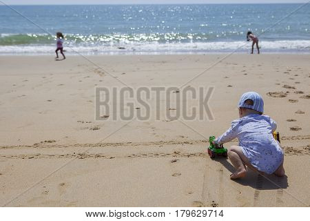 Baby boy playing on the sand while other children run beside shore beach. El Rompido Cartaya Huelva Spain