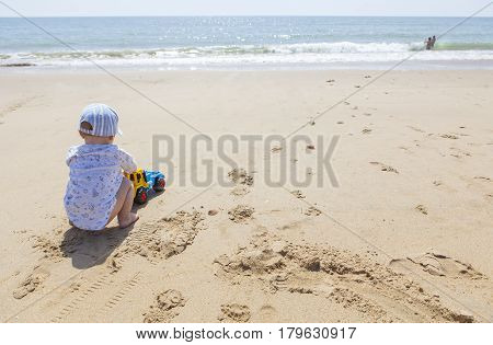Baby boy playing on the sand while other children splash beside beach shore. El Rompido Cartaya Huelva Spain