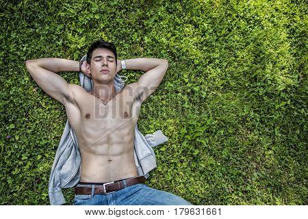 Good looking, shirtless fit male model relaxing lying on the grass, shot from above