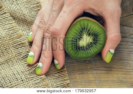 Kiwi and skin care of a beauty female hand with green and white moon nail art manicure on a sackcloth and wooden background