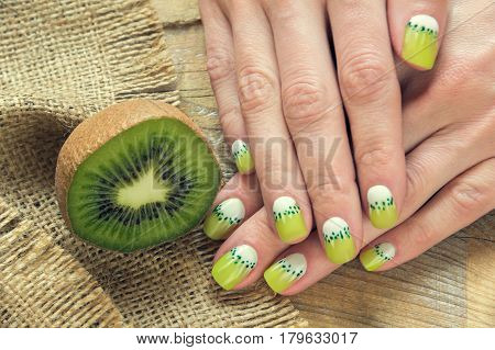 Kiwi and skin care of a beauty female hands with green and white moon nail art manicure on a sackcloth and wooden background