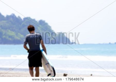 Surfer with board walks along the beach in blurred for background