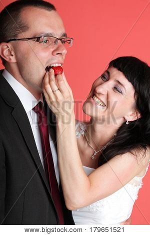 Happy smiling bride and groom young happy couple playfully eating strawbery on red background