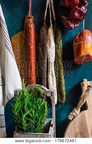 Variety of Spanish cured meat products charcuterie fresh rosemary wood cutting board hanging on hooks pantry