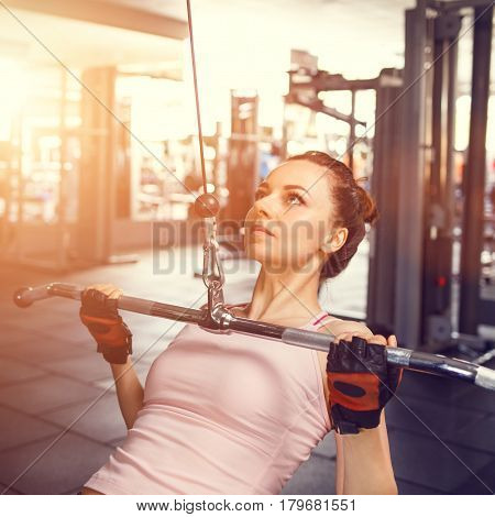 Young fitness woman performing close grip lat pulldown on cable machine