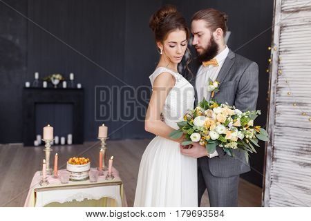 The bride with a bouquet in her hand and the groom stand side by side in a beautiful interior. Focus on the bride. Horizontal photo