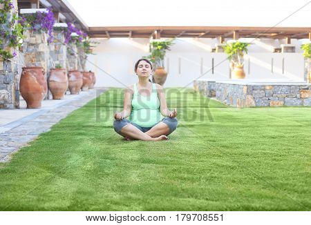 Beautiful pregnant woman meditaiting in summer park. Pregnant yoga