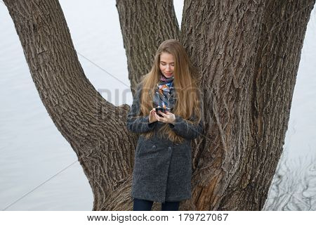 Portrait Of A Beautiful Girl With A Phone In Early Spring Outdoors.