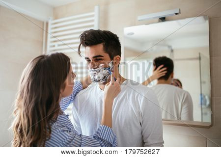 A handsome young man shaving in the bathroom.