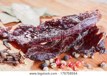 Pieces of beef jerky and spices on a wooden board