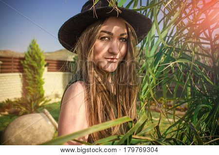 Young beautiful girl in a black hat and long dressin the sunny garden