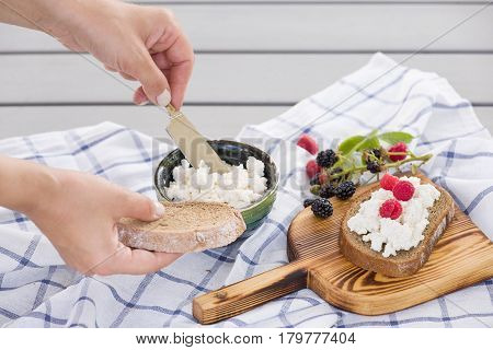 Woman taking organic farming cottage cheese from green bowl. Breakfast: slice of whole wheat bread with Homemade Ricotta cheese served with raspberries and blackberries on wooden board on linen fabric