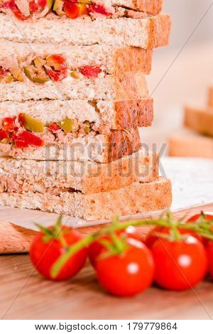 Tuna olives and tomato sandwiches on cutting board.