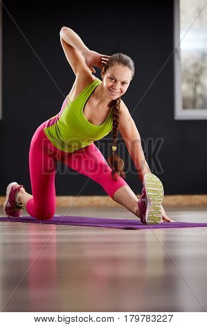 Slim athletic woman working out in gym doing knee-bounce exercise or lunges. Yoga woman in the sporty clothes, pink leggings and green t-shirt. On the violet yoga mat.
