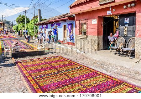 Antigua, Guatemala - March 26 2017: Locals make dyed sawdust procession carpets during Lent against backdrop of Agua volcano in colonial town with most famous Holy Week celebrations in Latin America.