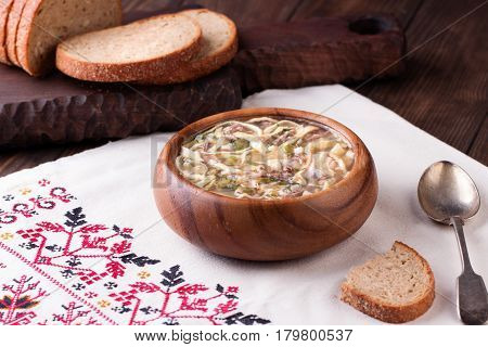 Traditional russian Cold Soup Okroshka with meat, vegetables and kvass serving size in wooden bowl and rye bread on wooden table. Kvass is a traditional Slavic and Baltic fermented beverage commonly made from rye bread