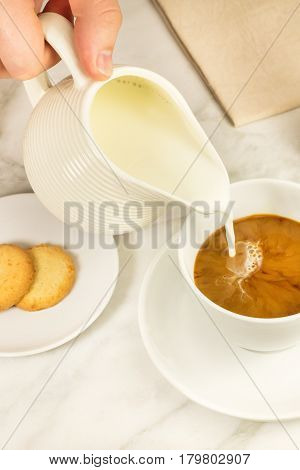 A photo of milk being poured into a cup of coffee. Selective focus, toned image