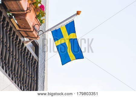 Flag of Sweden waving above the balcony of a building, blue sky behind.