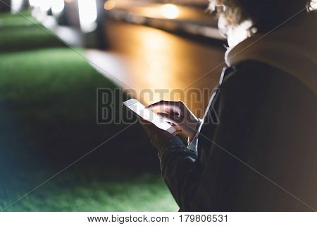 Girl pointing finger on screen smartphone on background illumination bokeh color light in night atmospheric city hipster using in female hands and texting mobile phone mockup glitter street content lifestyle
