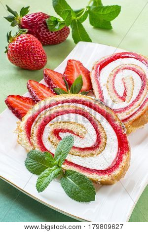Delicious cake roll with strawberry marmalade and marshmallow. Sliced rolls on a plate fresh strawberry and mint. Tasty fruit dessert. Vertical selective focus