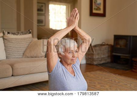 Active and focused senior woman doing the easy pose while practicing yoga alone in her living room at home