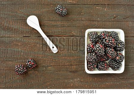 Blackberry fruit on wood background. Forest fruit in white idaeus and spoon. Delicious fresh berries.
