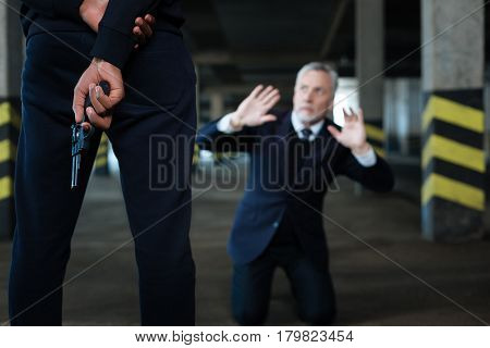 Do not kill me. Selective focus of a handgun being held behind the back of a dangerous aggressive kidnapper