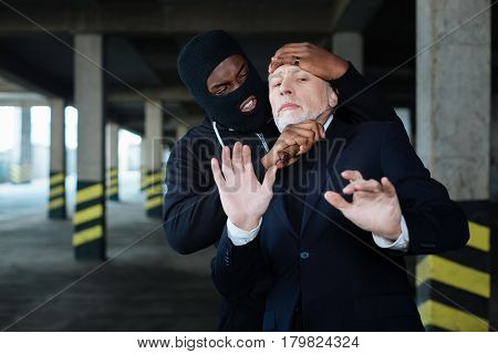 Committing a murder. Angry aggressive ruthless criminal holding a knife and holding a businessman while trying to kill him