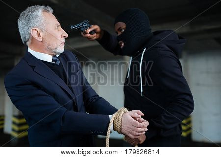 Give me money. Greedy strong male robber using a handgun and holding the rope while demanding money