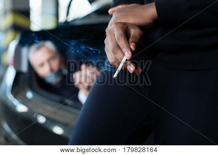 Tobacco product. Selective focus of a half smoked cigarette being in hands of a smart dangerous criminal