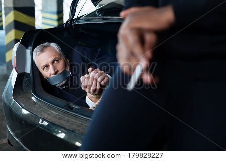 I will remember you. Sad angry unhappy businessman lying in his car boot and looking at his kidnapper while thinking how to get out