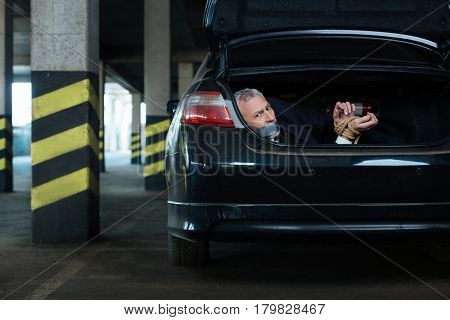 Help me. Scared worried grey haired man having adhesive tape over his mouth and not being able to speak while lying in the car boot