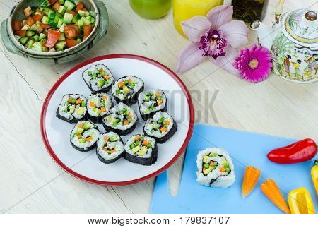 Home made vegan sushi rolls on a plate and vegetables on a blue board