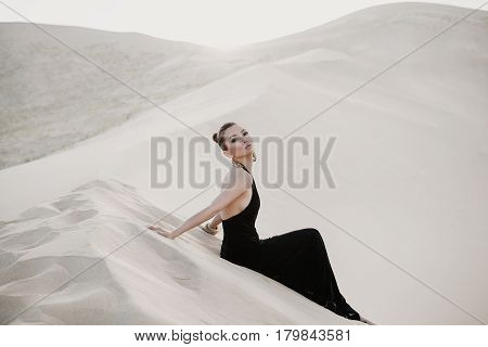 Woman model in a black dress is posing in desert