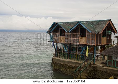 Wooden house on piles in shallow sea water. Traditional house in Philippines. Seaside scene with eco lodge in sea. Minimalist resort banner template with text place. Philippines island hopping travel