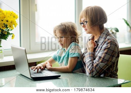 The grandmother and the grandson with interest look at the laptop screen. The elderly woman and the boy sit next. Modern technologies are available to people of all age.