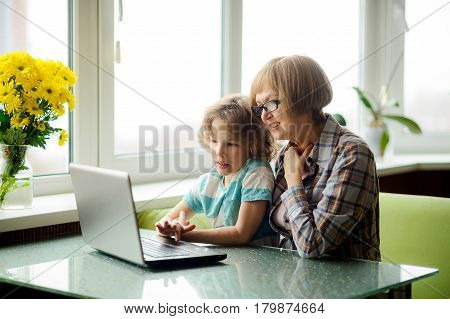 The grandmother and the grandson with interest look at the laptop screen. The elderly woman and the boy sit next. Modern technologies are available to people of all age.