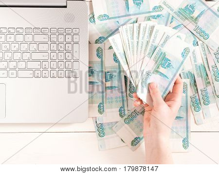 Hand holding russian rubles near laptop on table with banknotes. Top view or flat lay. Finance and earning concept