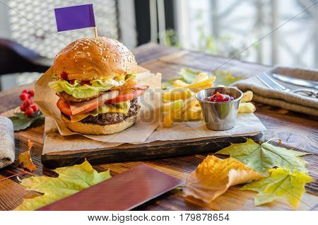 Homemade beef burger. Beef cheese tomatoes onion green salad Tabasco sauce and French fries on a wooden table