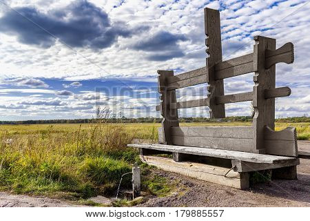 Old bench with clear water in the spring against the background of the field and sky