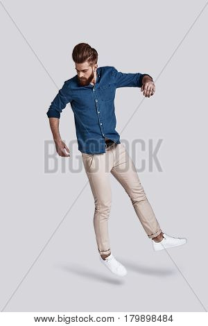 Man in mid-air. Full length of handsome young man looking down while jumping against grey background
