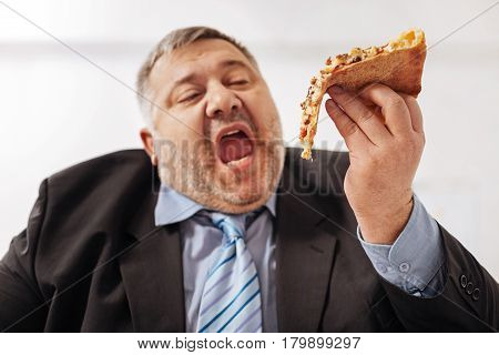 Worshiping food. Excited hungry unhealthy guy enjoying eating junk food while having a lunch break in the office