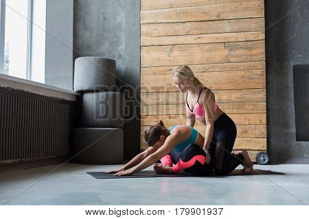 Yoga class instructor helps beginner to make asana exercises. Teacher assists to make cobbler pose, baddha konasana. Healthy lifestyle in fitness club. Stretching with coach